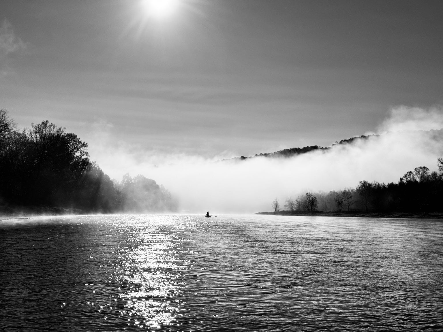A lone drift boat on a misty Arkansas river